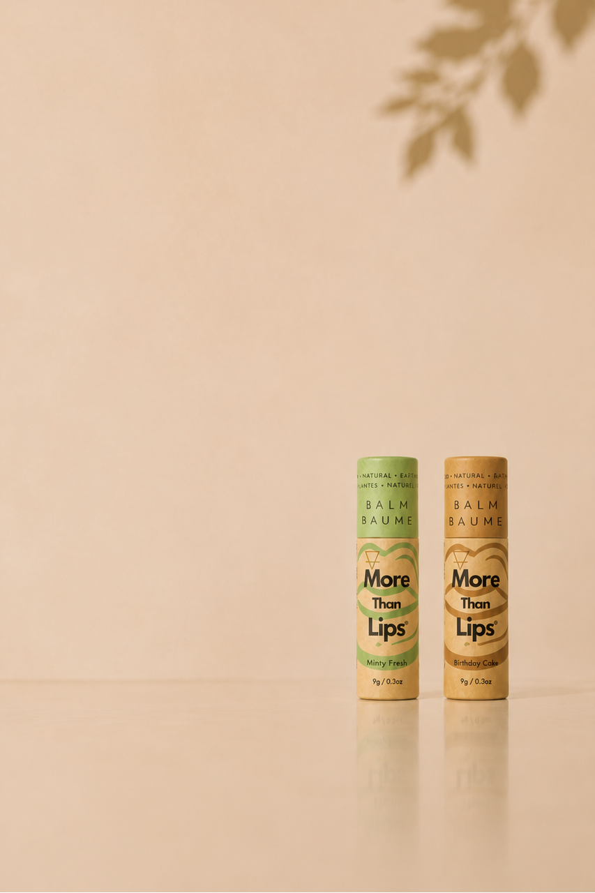 Two tubes of Mona Lisa Lips balmy lip balm standing upright on a beige surface against a warm beige background with a leaf shadow cast on the wall.